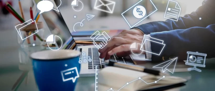Persona escribiendo en una laptop con gráficos y símbolos de comunicación, finanzas y análisis de datos en el fondo, junto a una taza de café y material de oficina.